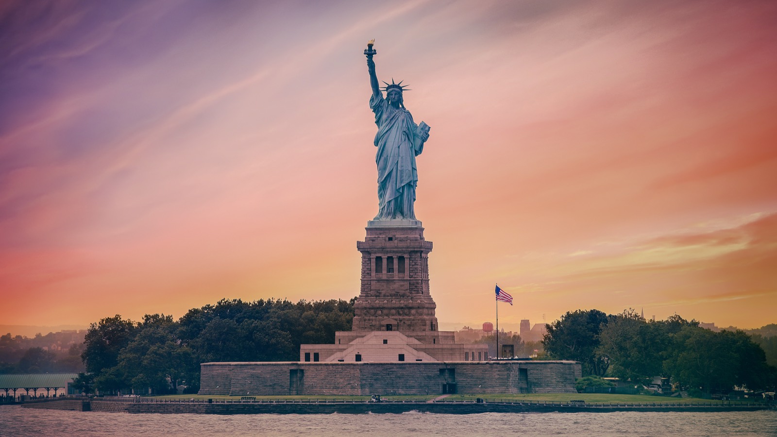 The Statue of Liberty at sunset, its copper-green surface glowing against a warm orange sky